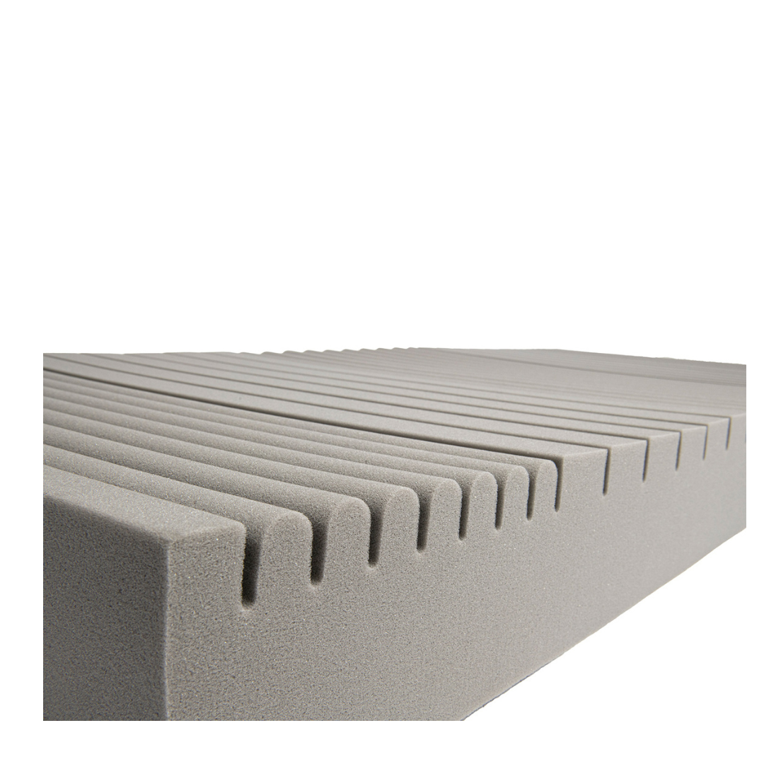 A close-up of the Proactive Protekt® 100 Pressure Redistribution Foam Mattress shows its gray, high-resilience foam block with evenly spaced parallel grooves, set against a white background.