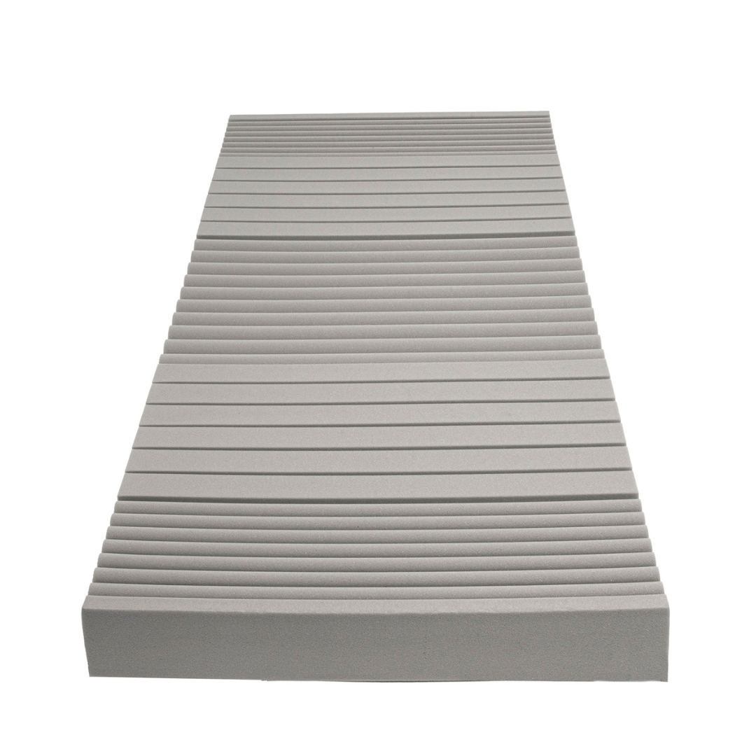 A rectangular Proactive Protekt® 100 Pressure Redistribution Foam Mattress in gray high-resilience foam features evenly spaced horizontal grooves, shown from a low angle.