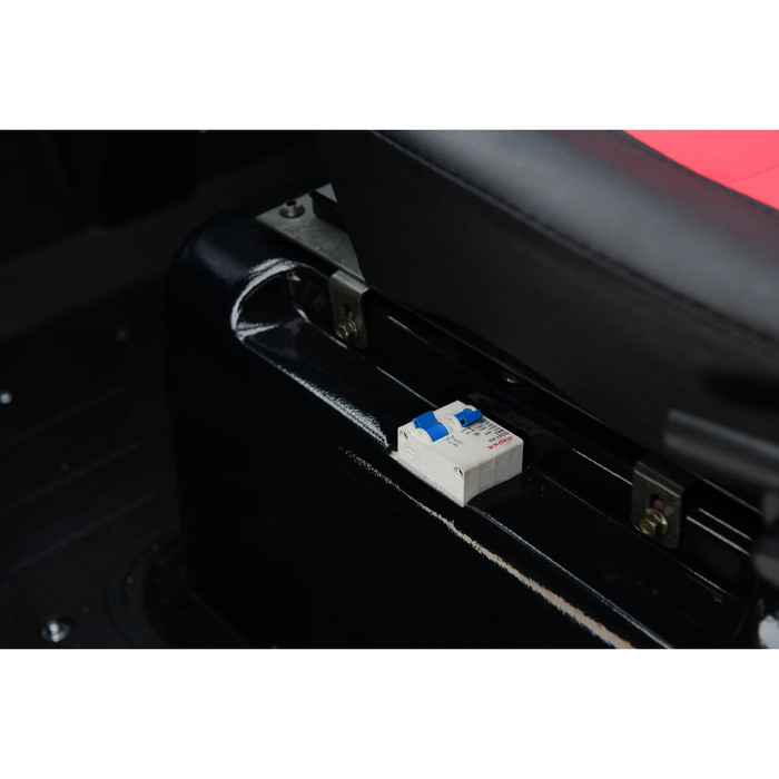 A close-up of a small electrical circuit breaker with a blue switch, mounted under the seat of a Green Transporter Q Express Fully Enclosed Scooter with red and black upholstery.