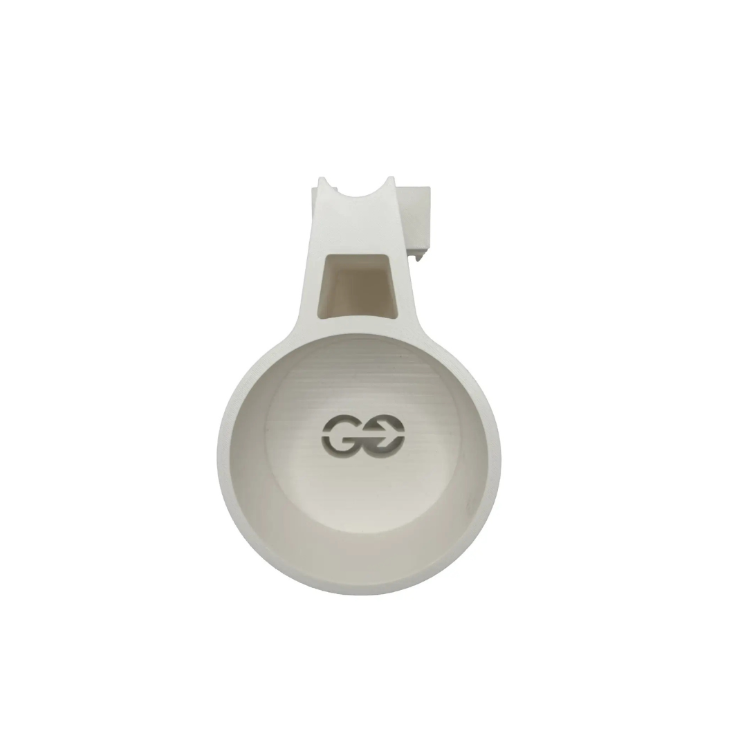 A white, round plastic Quick Detach Oxygen E Tank Holder for ComfyGo Powerchairs with a handle featuring a rectangular cutout. Viewed from above, two black arrows point toward each other inside. Background is plain white.