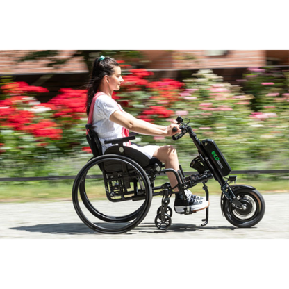 A woman rides outdoors in a manual wheelchair with the Rehasense ECO Assist Power Chair Conversion System, surrounded by blurred red and pink flowers, highlighting the added movement and speed this innovative mobility solution provides.