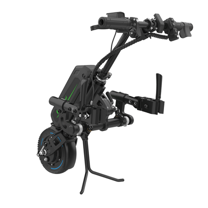 The Rehasense ECO Travel LX Power Add-On – Lightweight Wheelchair Motor Assist is a black device with handlebars, single front wheel, battery pack, brake levers, and support stands that converts a manual wheelchair into a powered tricycle.