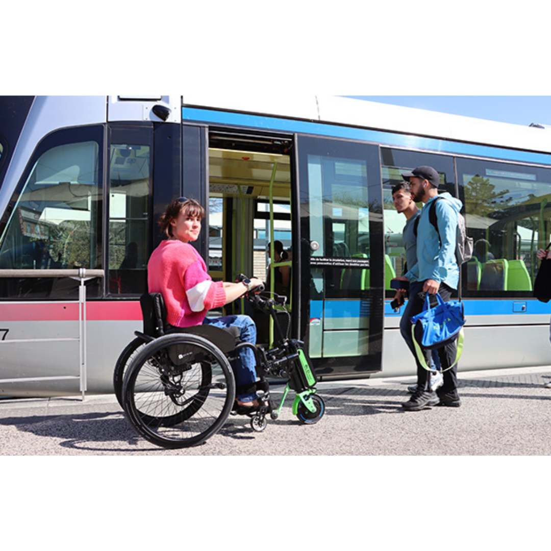 A woman using a Rehasense ECO Travel LX Power Add-On – Lightweight Wheelchair Motor Assist gets ready to board a modern tram as two men with bags exit. The tram is stopped outdoors during the day, its doors wide open.