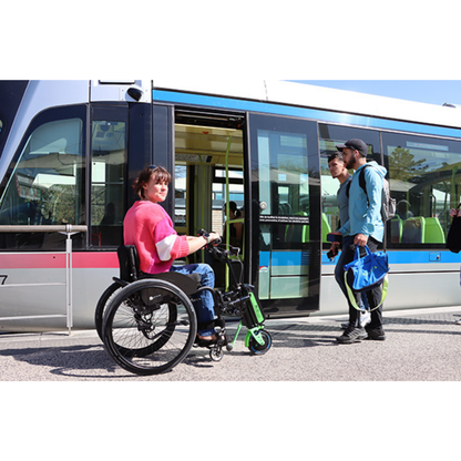A woman using a Rehasense ECO Travel LX Power Add-On – Lightweight Wheelchair Motor Assist gets ready to board a modern tram as two men with bags exit. The tram is stopped outdoors during the day, its doors wide open.