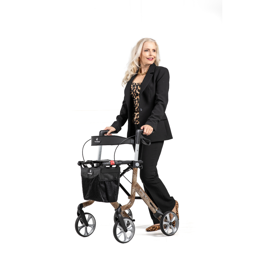 A woman with long white hair in a black suit and leopard-print shoes stands using a Rehasense Space LX Designer Ultralight Rollator with leopard-print accents, against a plain white background.