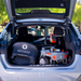 The image features the open trunk of a silver car containing a folded black stroller labeled REYHEE, a silver toy car with a steering wheel, and the Reyhee Cruiser Portable Electric Mobility Scooter with Front Basket. Blurred greenery and parked cars are visible in the background.