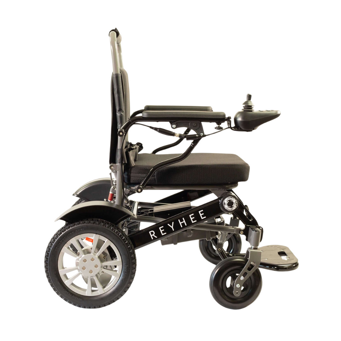 Side view of a black folding electric wheelchair, the Reyhee Roamer, with the brand name on the lower frame. This FDA-cleared mobility device has joystick control on the right armrest, large rear and smaller front wheels, and a foldable footrest.