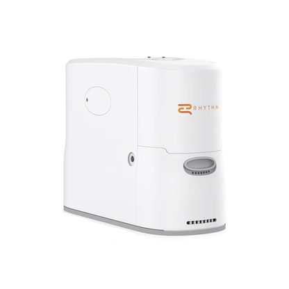 The Rhythm Oxygen Concentrator Premium Bundle is a white, rectangular device with rounded edges, "Rhythm" in orange on the front, various ports, and a base vent, shown against a plain white background.