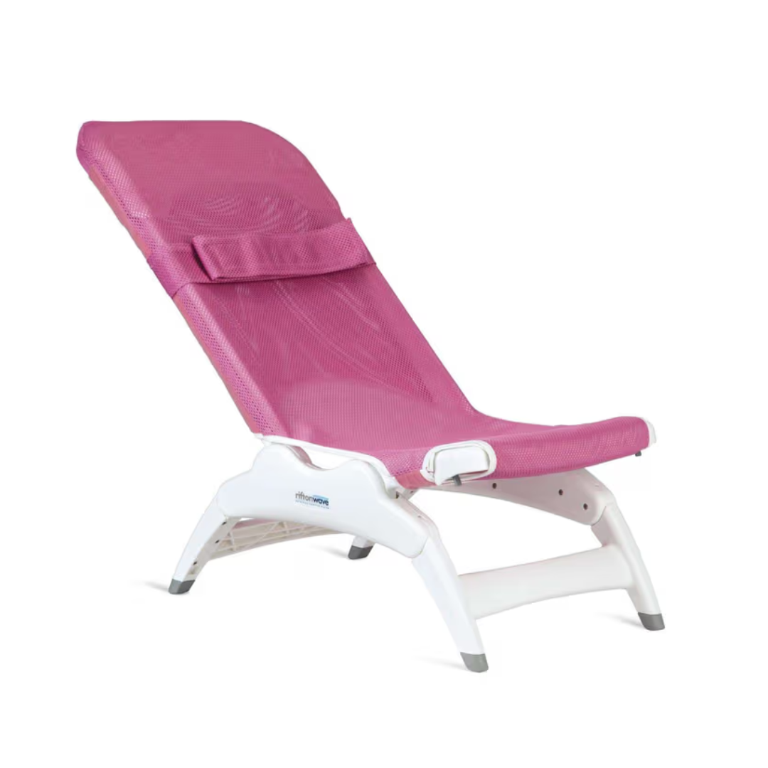 The Rifton Wave Pediatric Shower Chair is a pink mesh lounge chair with a white plastic frame, headrest, and angled backrest for comfortable reclining—similar to an adjustable shower chair.