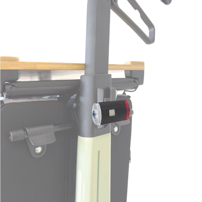 Close-up of the Light For The Rollz Air Rollator, an attachable black and red LED flashlight fixed to a Rollz Air Rollator’s pole, with a wooden surface and fabric bag in the background.