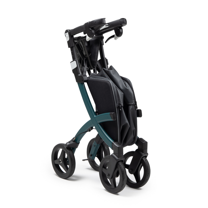 A folded Rollz FLEX 2 Lightweight Rollator Walker in teal and black is shown upright with four wheels, featuring a compact design for easy storage and transport. It has a basic frame, a handlebar for pushing, and includes an XL storage bag underneath.