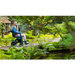 A person using the Rollz Motion Performance All-Terrain 2-In-1 Rollator Transport Chair smiles while exploring a lush garden. The air-filled tires and dirt pathway are surrounded by green ferns and trees, creating a serene atmosphere with excellent shock absorption for a smooth journey.