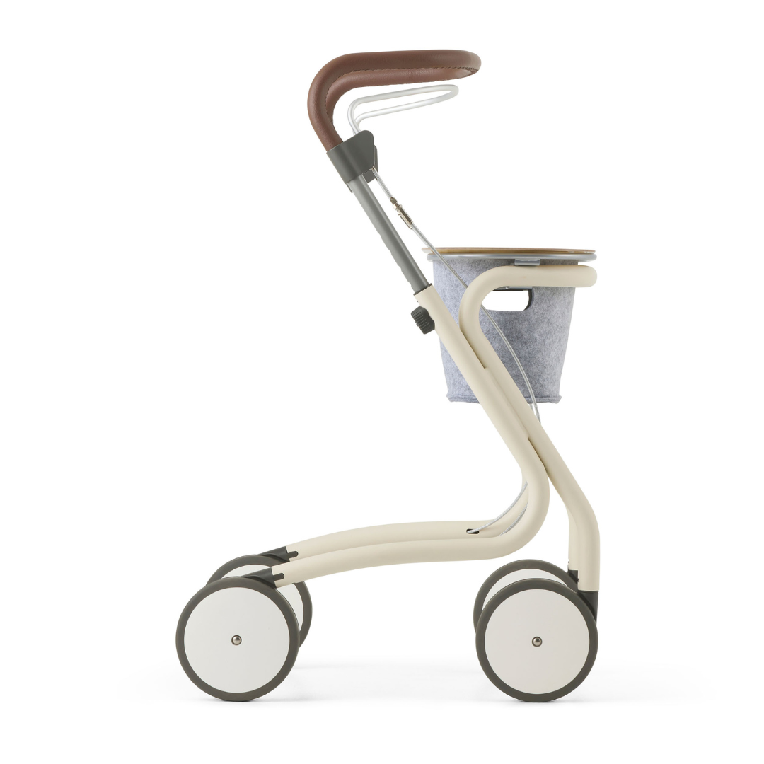 The byACRE Scandinavian Butler At-Home Rollator features four large wheels, a curved beige frame, brown handlebar, and small gray fabric basket—offering modern, minimalist Scandinavian style for elegant daily mobility.