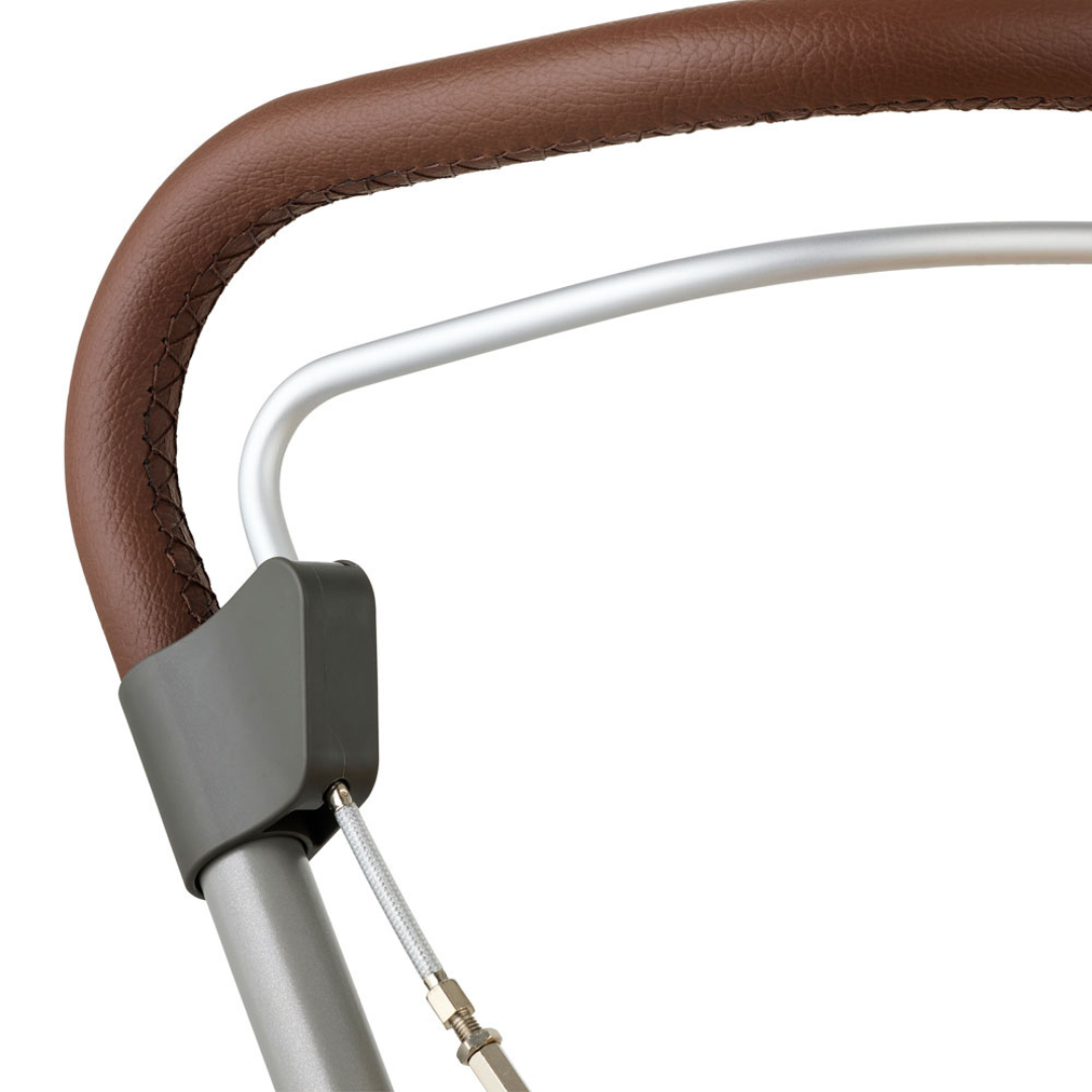 Close-up of the byACRE Scandinavian Butler At-Home Rollator’s handle, wrapped in brown leather with visible stitching, a gray plastic connector, metal frame, and slim wire cable—highlighting its refined Scandinavian design.
