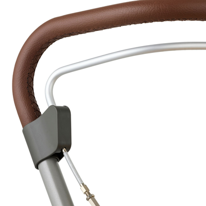 Close-up of the byACRE Scandinavian Butler At-Home Rollator’s handle, wrapped in brown leather with visible stitching, a gray plastic connector, metal frame, and slim wire cable—highlighting its refined Scandinavian design.