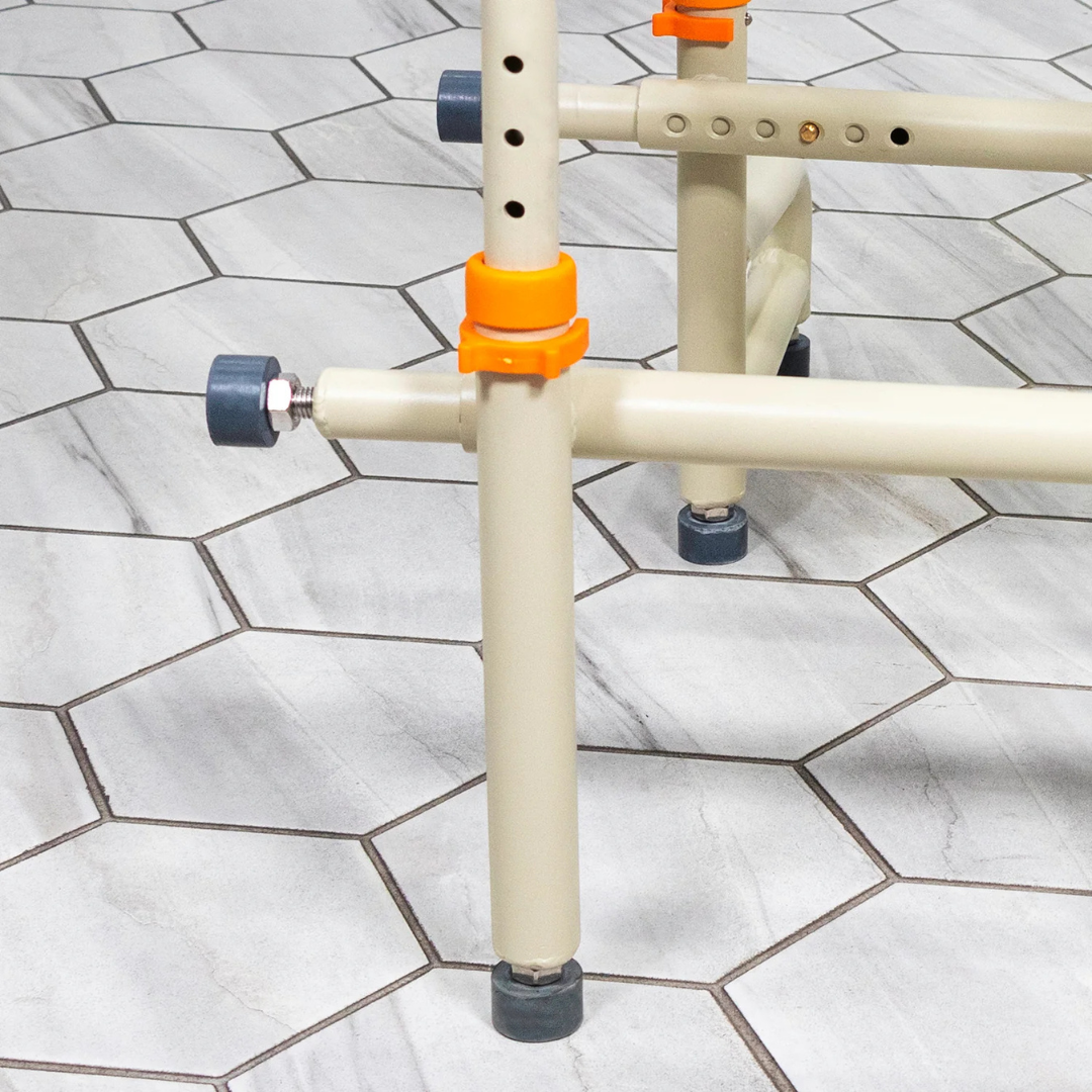Beige metal frame with gray rubber feet and orange adjustable clamps, part of the ShowerBuddy SB2T TubBuddy with Tilt, positioned on a floor with light gray hexagonal tiles.