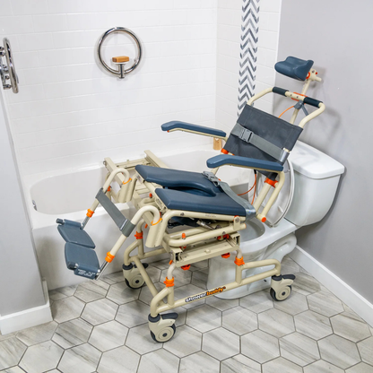 The ShowerBuddy SB2T TubBuddy with Tilt, a beige and gray shower chair with footrests, is positioned over a toilet and partially inside a bathtub in a modern bathroom with tile flooring.