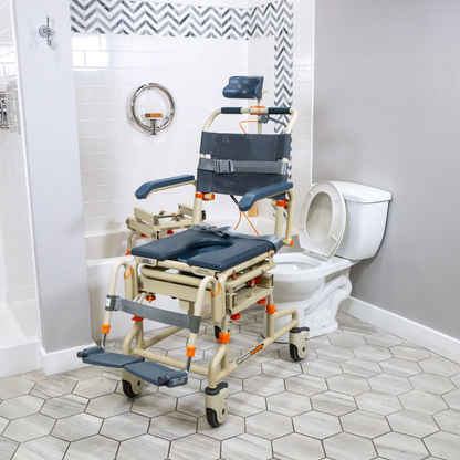 A beige and gray ShowerBuddy SB2T TubBuddy with Tilt rolling shower chair is positioned over a white toilet in a modern, accessible bathroom with tiled floors and walls.