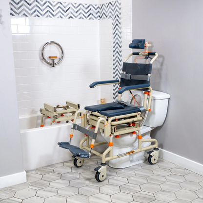 The ShowerBuddy SB2T TubBuddy with Tilt is positioned over a toilet beside a bathtub with a grab bar and bath transfer bench in a tiled bathroom, creating an accessible bathing system.