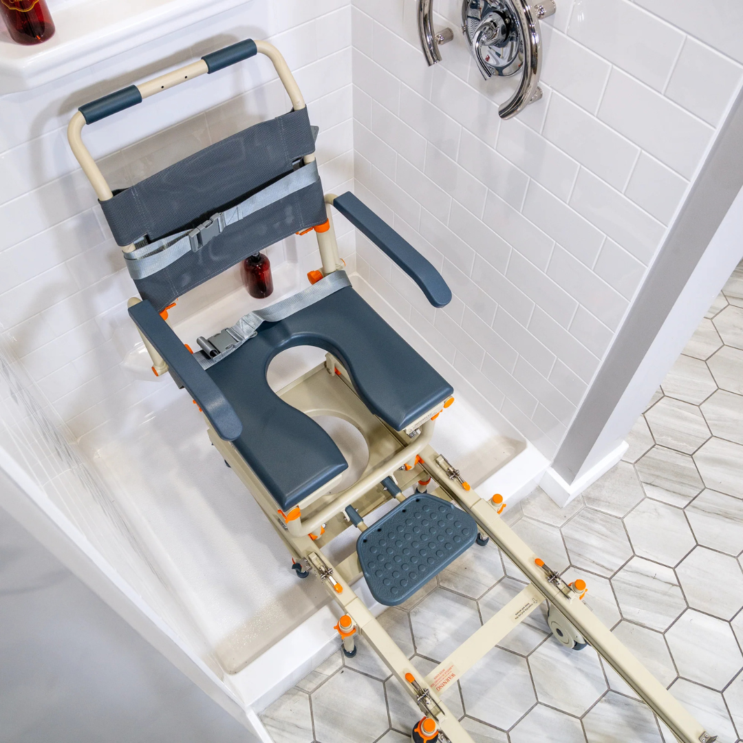 The ShowerBuddy® SB1 Transfer System with Rolling Shower Chair features a cutout seat, armrests, and a sliding track for easy shower transfers over the lip onto a hexagonal-tiled bathroom floor.