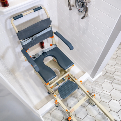 The ShowerBuddy® SB1 Transfer System with Rolling Shower Chair features a cutout seat, armrests, and a sliding track for easy shower transfers over the lip onto a hexagonal-tiled bathroom floor.