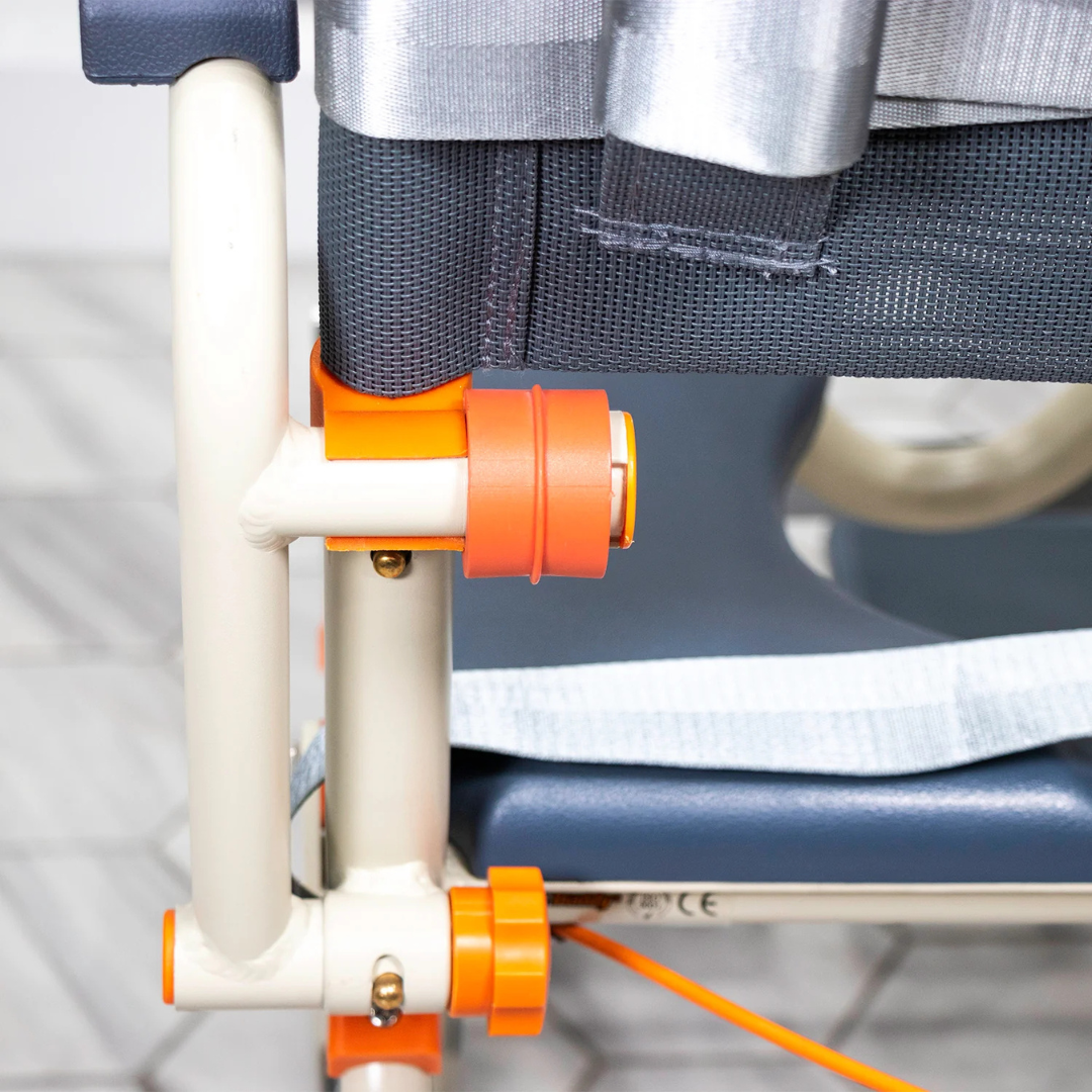 Close-up of the ShowerBuddy SB3T Roll-In Shower Chair with Tilt Recline, featuring a metal frame, orange adjustment knobs, and gray fabric seat, shown on a tiled floor.
