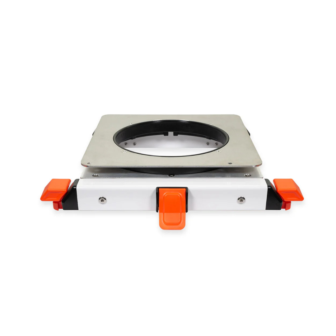A square metal mounting bracket with a circular center hole, featuring orange and black clips—designed as an accessory for ShowerGlyde® Transfer Benches to securely fit a hard-plastic seat and improve bathing comfort.