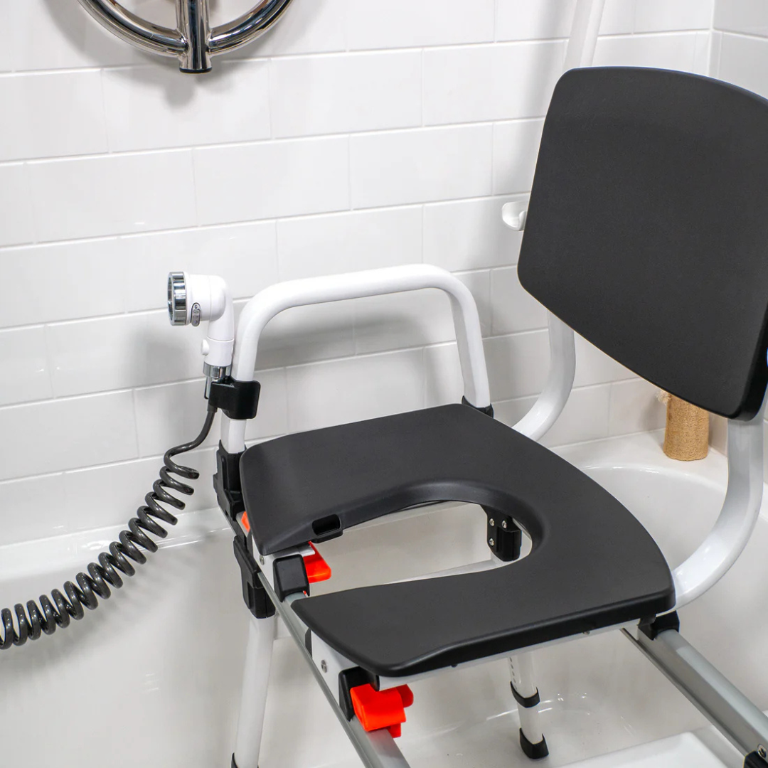 Accessories and Parts for ShowerGlyde® Transfer Benches, featuring a hard-plastic, open seat design with backrest and armrests, are shown in a tiled bathroom with a nearby handheld showerhead and flexible hose for added comfort.
