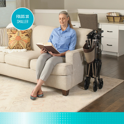 A smiling older woman relaxes on a beige sofa, reading with her Signature Life Elite Travel Rollator folded beside her. The room is bright and cozy, featuring a decorative pillow and desk. Text reads: FOLDS 3X SMALLER.