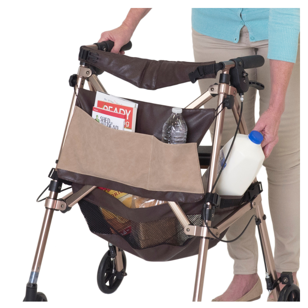 A person puts a milk jug into a tan and brown walker bag attached to the Signature Life Elite Travel Rollator, which also holds books, a water bottle, and groceries. The person wears beige pants and a light blue sweater.