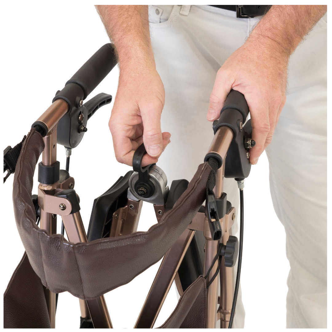 A person adjusts a knob on the Signature Life Elite Travel Rollator, featuring brown handles and a storage pouch, while wearing light-colored pants and a light shirt.