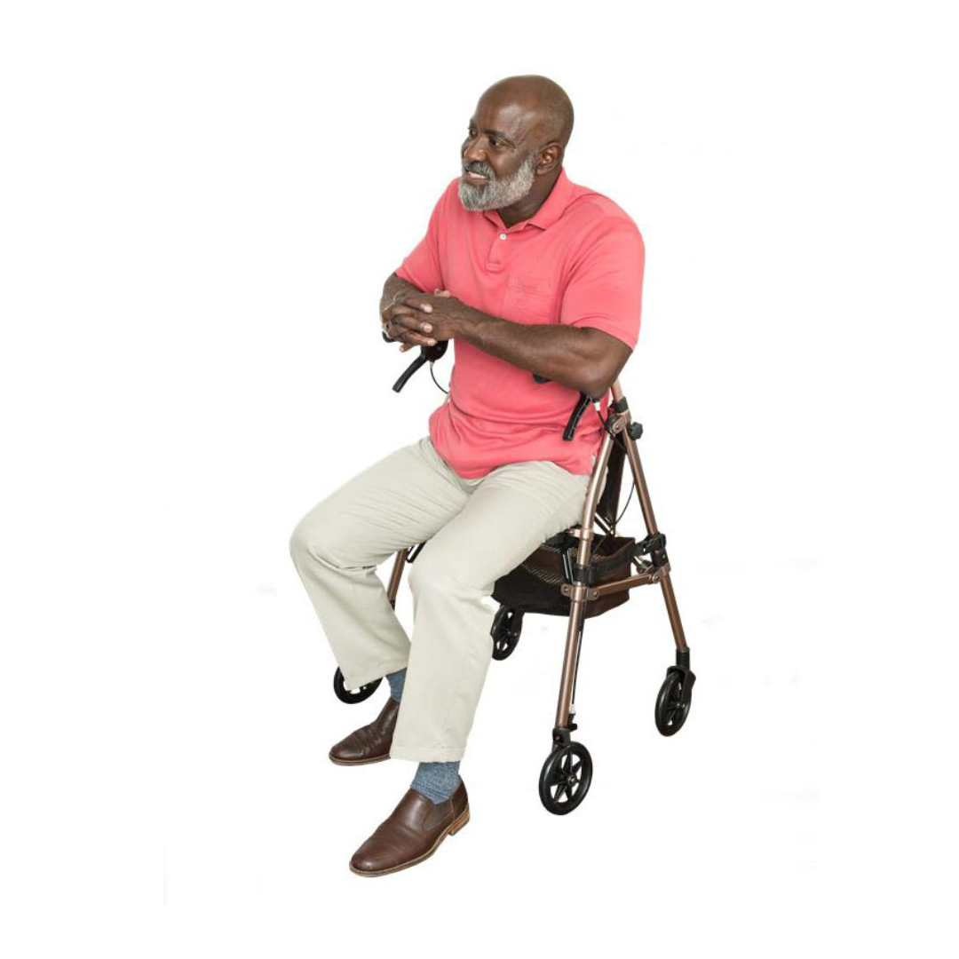 A man with a gray beard, in a pink polo and light pants, sits on the Signature Life Elite Travel Rollator with built-in seat, hands on the handle, against a white background.