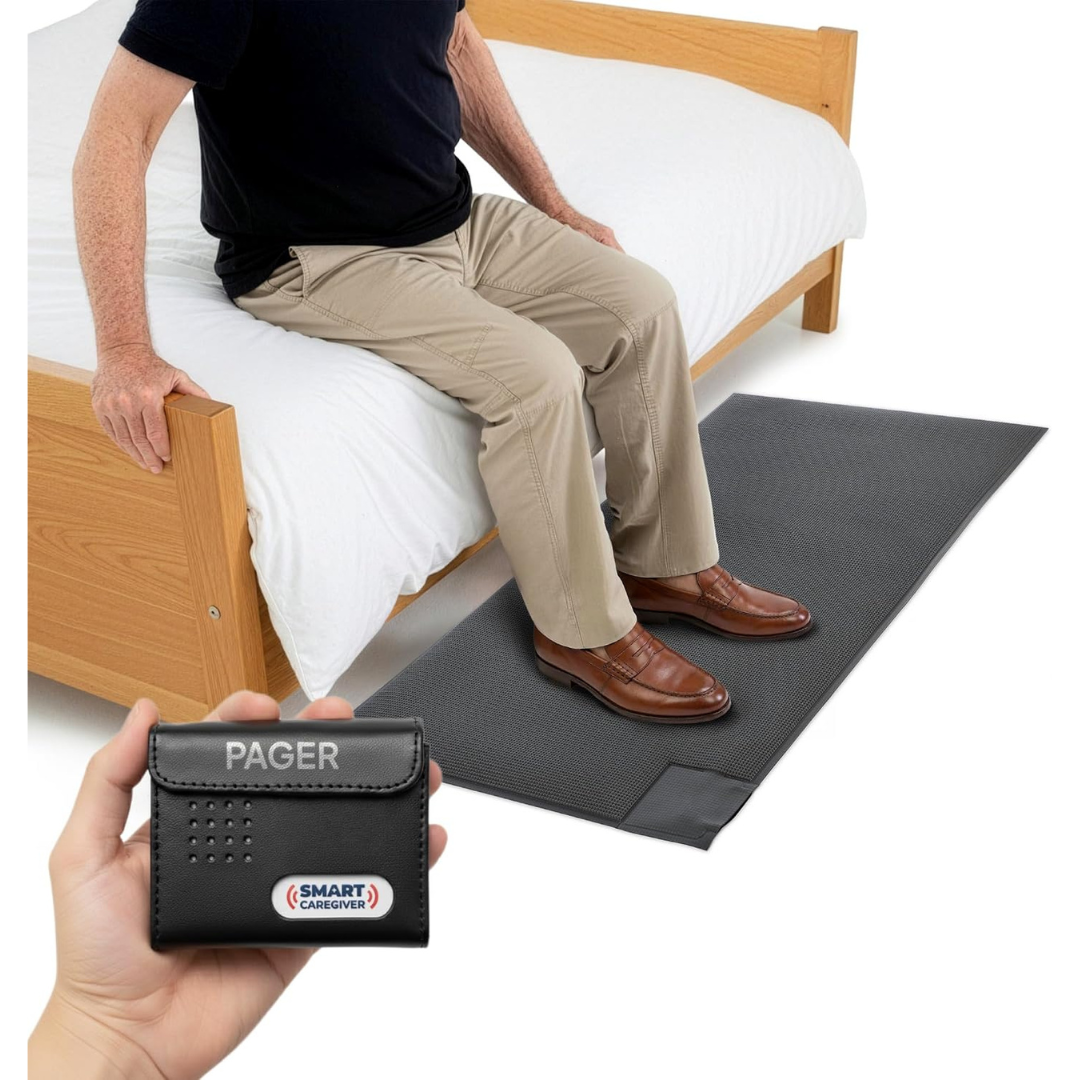 A person sits on the edge of a bed with their feet resting on a gray floor mat, while a hand holds a SmartCaregiver Pager device. The scene features the SmartCaregiver Pager Bed/Chair Exit Alert & Systems, designed for effective safety monitoring and fall prevention.