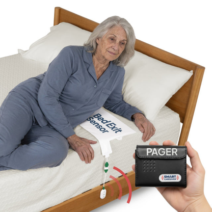 An elderly woman in pajamas is lying on a bed next to a Bed Exit Sensor pad, while a hand holds the SmartCaregiver Pager from the SmartCaregiver Pager Bed/Chair Exit Alert & Systems, with red signal lines depicting wireless connectivity as part of the alert system.