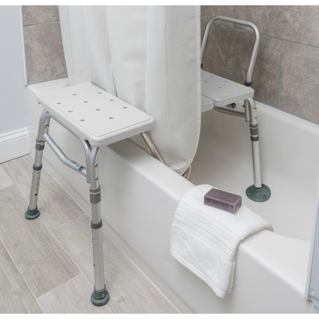 The Drive Splash Defense™ Transfer Bench with Curtain Guard Protection features adjustable legs for seniors, straddles the tub for bath safety, with part of the seat inside. A towel and soap rest nearby, while a shower curtain fits between the split seat design.