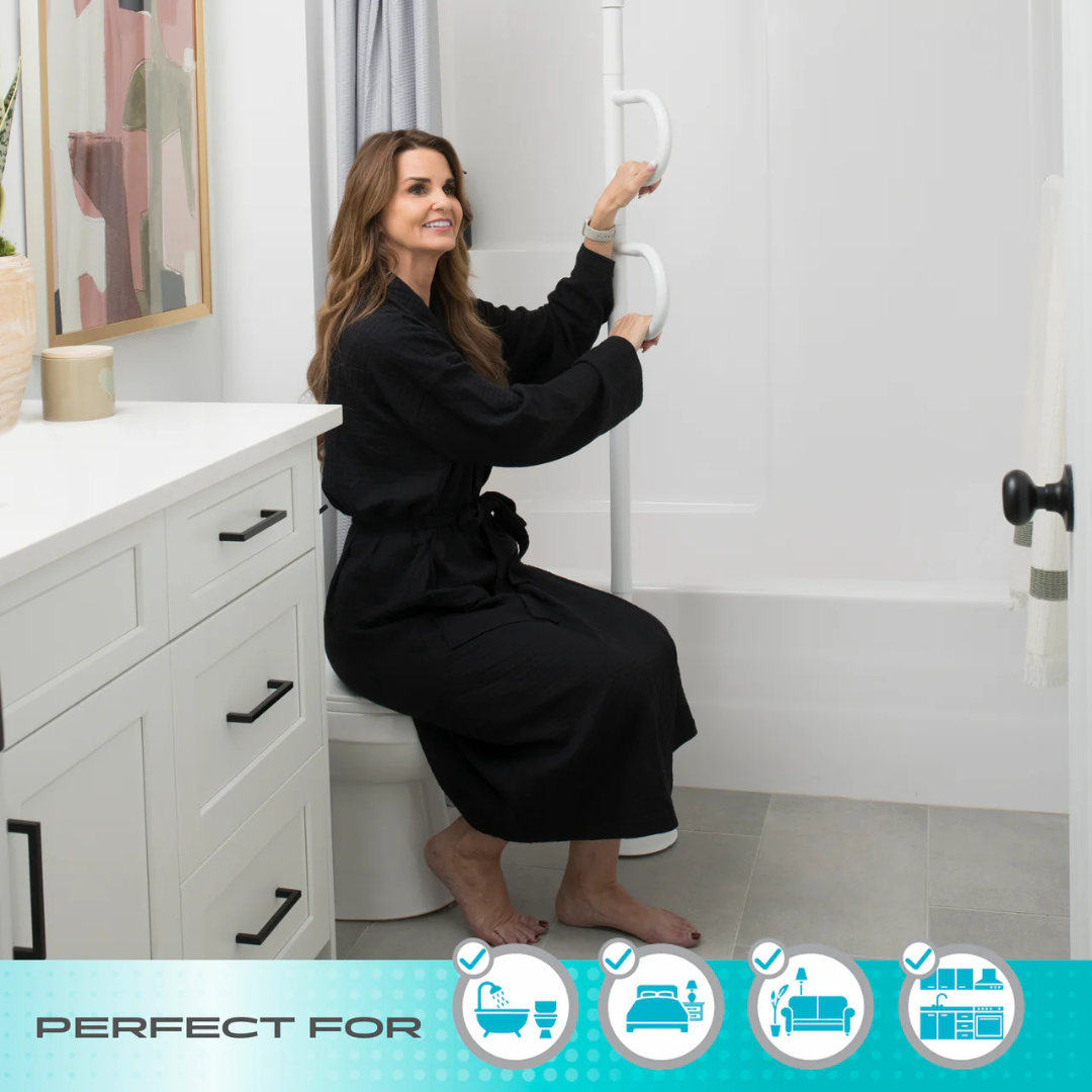 A woman in a black robe sits on a closed toilet, holding the Stander Double Handle Floor to Ceiling Grab Bar next to a bathtub. Icons show this grab bar is ideal for use by the bath, bed, couch, and chair in modern bathrooms.