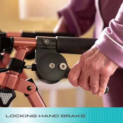 Close-up of an elderly hand gripping the locking hand brake of a rose gold Stander Space Saver Rollator - Ultra Compact & Lightweight, with "Locking Hand Brake" text shown at the bottom.
