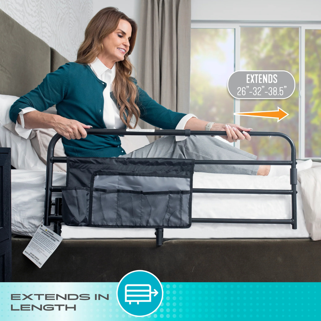 A woman sits on a bed adjusting a Stander Wonder Extendable Pivot Bed Rail with a storage pouch, which extends from 26 to 38.5 inches for added nighttime safety. The modern room features stylish decor and a large window.