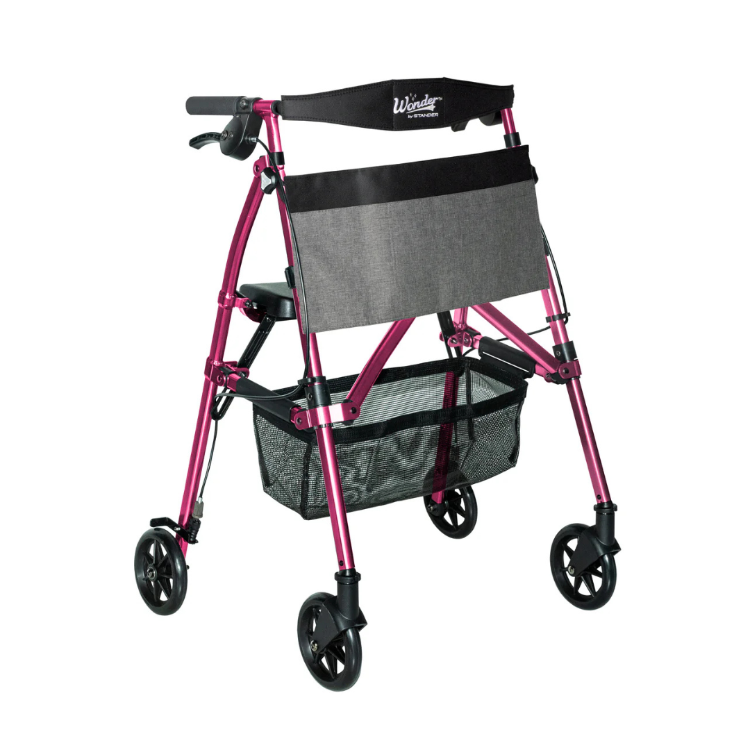 The Stander Wonder Rollator Plus is a pink compact folding walker with a black seat, grey front pouch, mesh basket below, and ergonomic handles—ideal for easy storage and travel.