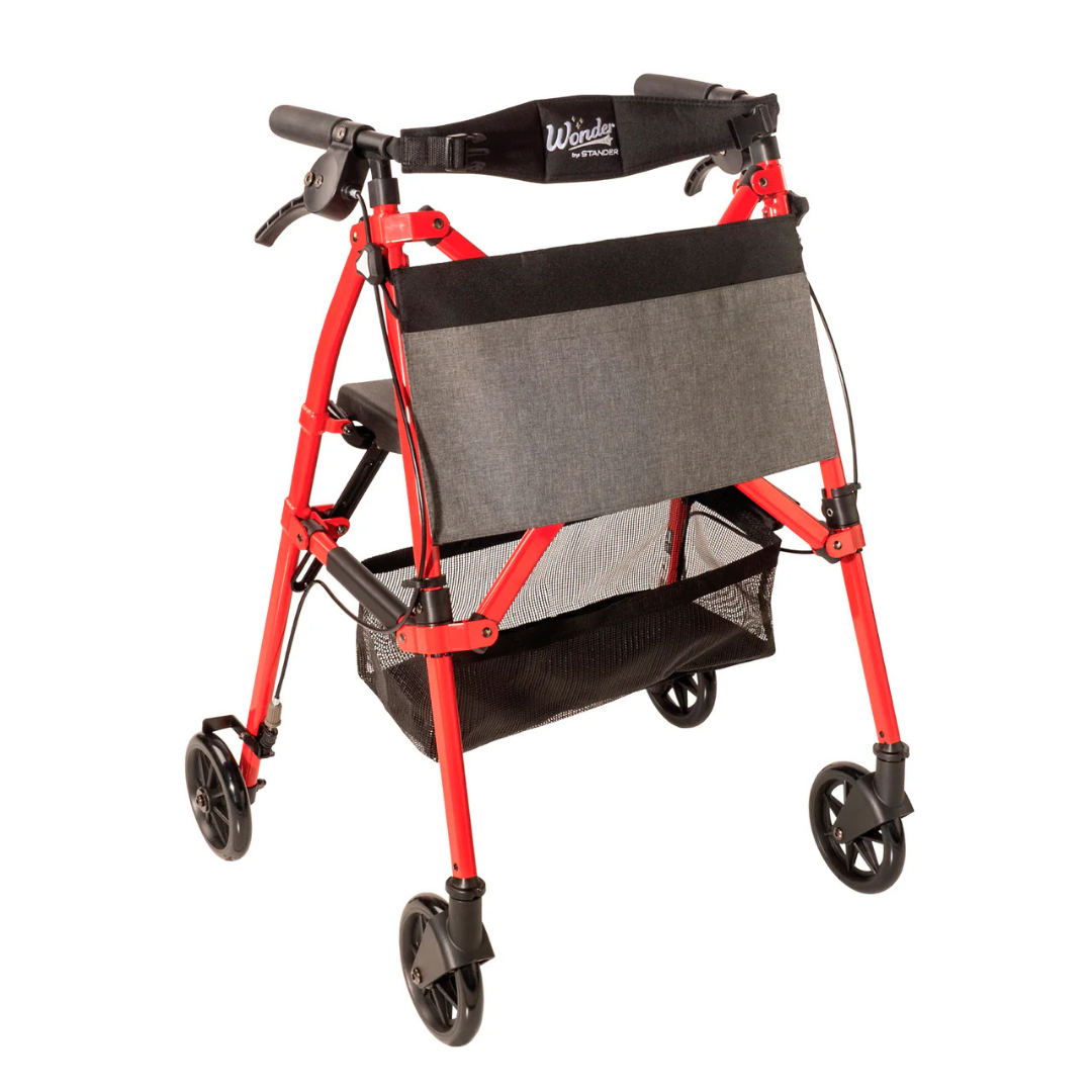 The Stander Wonder Rollator Plus is a red, four-wheeled travel rollator with a black seat, gray storage pouch, black mesh basket underneath, hand brakes, compact folding design, and “Wander” labeled on the backrest.