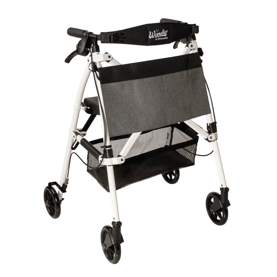 The Stander Wonder Rollator Plus is a lightweight, white, compact folding rollator with four black wheels, padded seat, mesh storage basket underneath, and a black backrest.