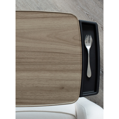 The Stander Wonder Tray Premium - XL TV Tray & Standing Aid is pictured from above, with a metal fork in its black tray, beside a rectangular light wood tabletop. A white chair and light wood floor are also visible.