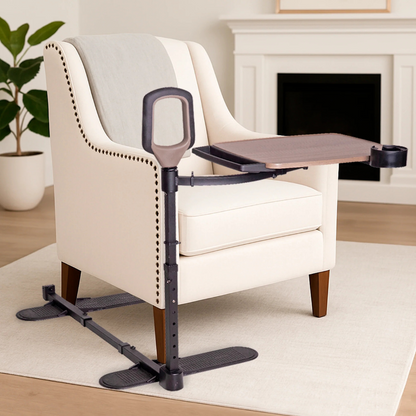The Stander Wonder Tray Premium - XL TV Tray & Standing Aid, a beige armchair accessory with dark-brown adjustable tray, stand assist handle, and cup holder, sits in a modern living room with a plant and fireplace in the background.