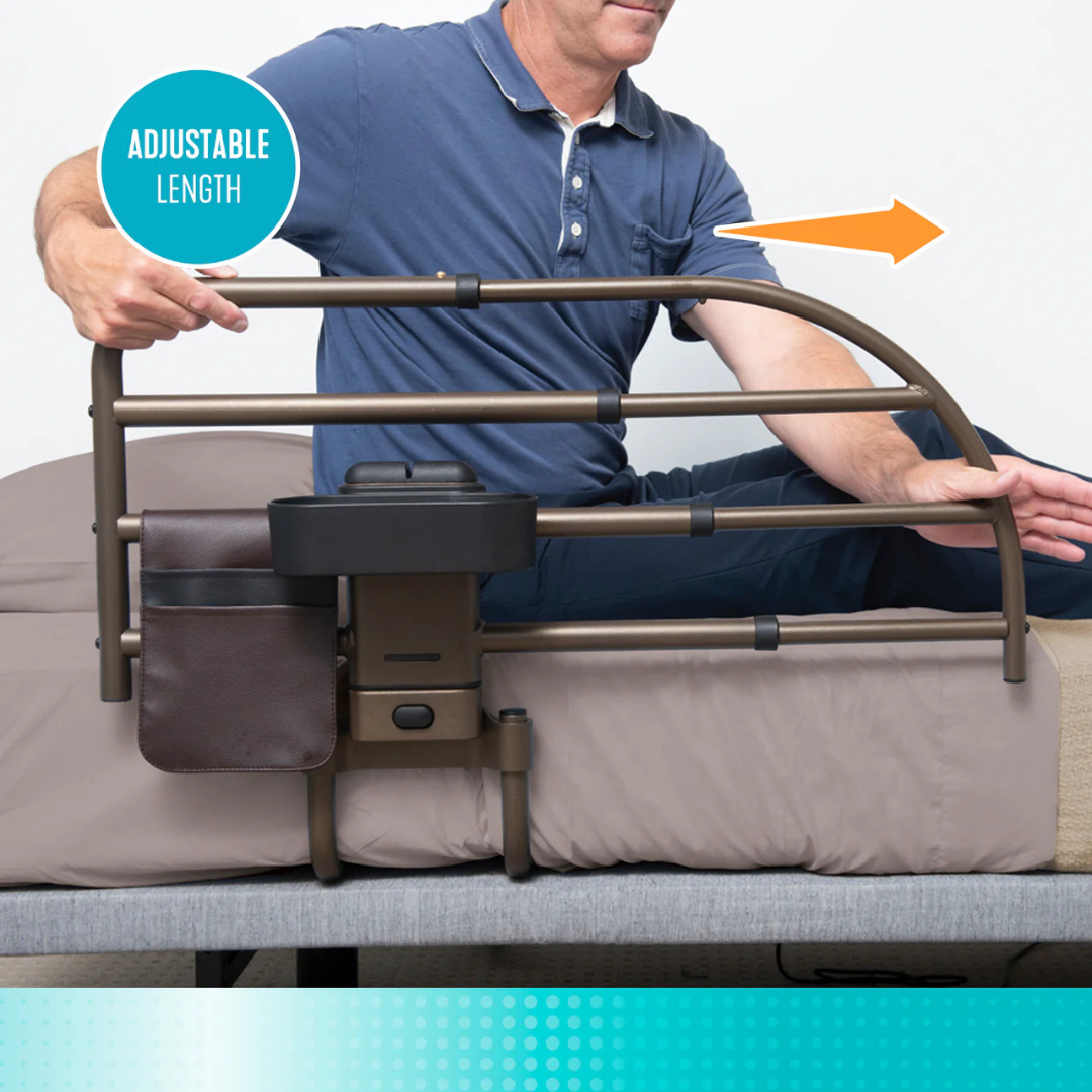 A man demonstrates the Signature Life Freedom Click Extendable Bed Rail attached to a bed, showing its rail extending or retracting for fall protection. The rail has a pouch, tray, and a label reading "ADJUSTABLE LENGTH" with an arrow indicating adjustability.