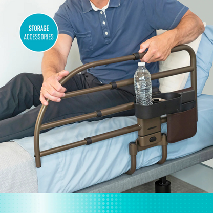 A person on a bed grips the Signature Life Freedom Click Extendable Bed Rail for fall protection, which includes storage accessories like a water bottle holder and pocket, beside blue and white bedding.
