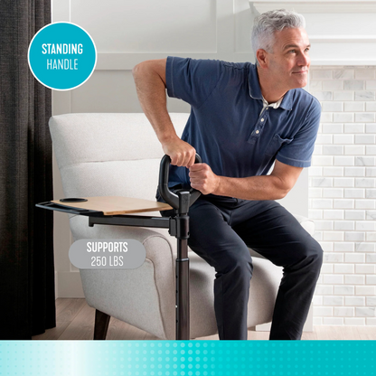 A man uses the Stander Assist-A-Tray Standing Aid With Swivel Tray, featuring a support handle and adjustable tray with cup holder, to help him stand up from an armchair. The handle supports up to 250 lbs.