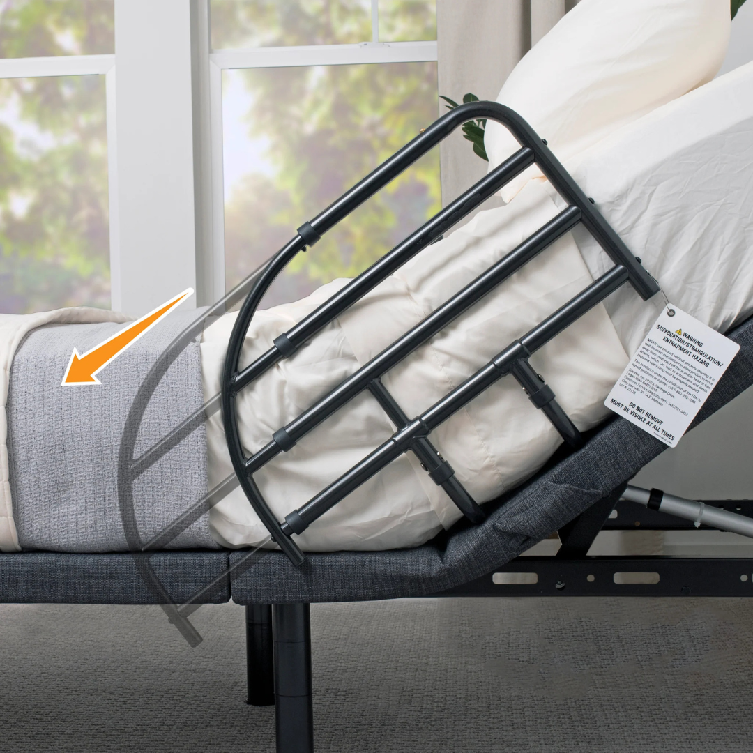 The Stander Wonder Extendable Bed Rail For Adjustable Beds, shown with a gray frame attached to the bed side, is highlighted by an orange arrow indicating its movement in a carpeted room with a window overlooking greenery.