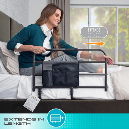 A woman adjusts the Stander Wonder EZ Adjust Bed Rail - Extendable on the side of a bed in a bright bedroom. A graphic shows that this extendable bed rail extends from 20 to 30 inches in length. Text at the bottom reads EXTENDS IN LENGTH.