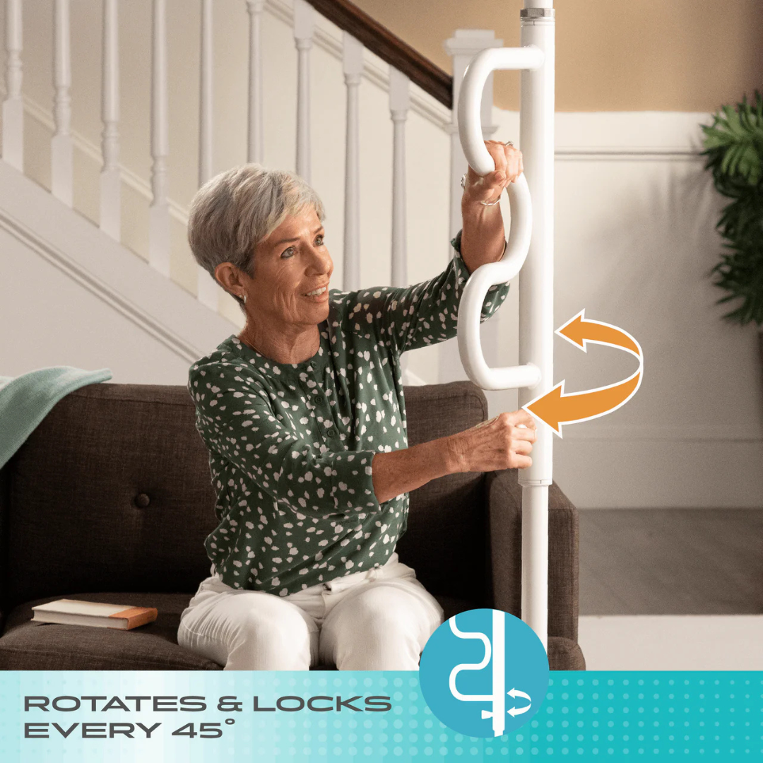 An older woman sits on a couch, holding the Stander Wonder Pole HD - Bariatric Fall Prevention Safety Pole. An arrow shows the grab bar rotates and locks every 45° for fall prevention.