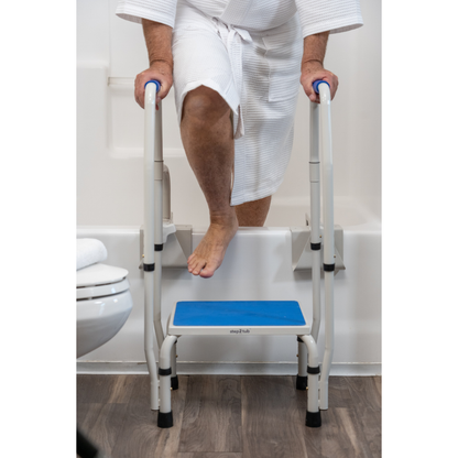 A person in a white robe uses the Step2Tub Bathtub Step Stool with handrails to safely step into or out of a bathtub in a bathroom with wood flooring, enhancing fall prevention.